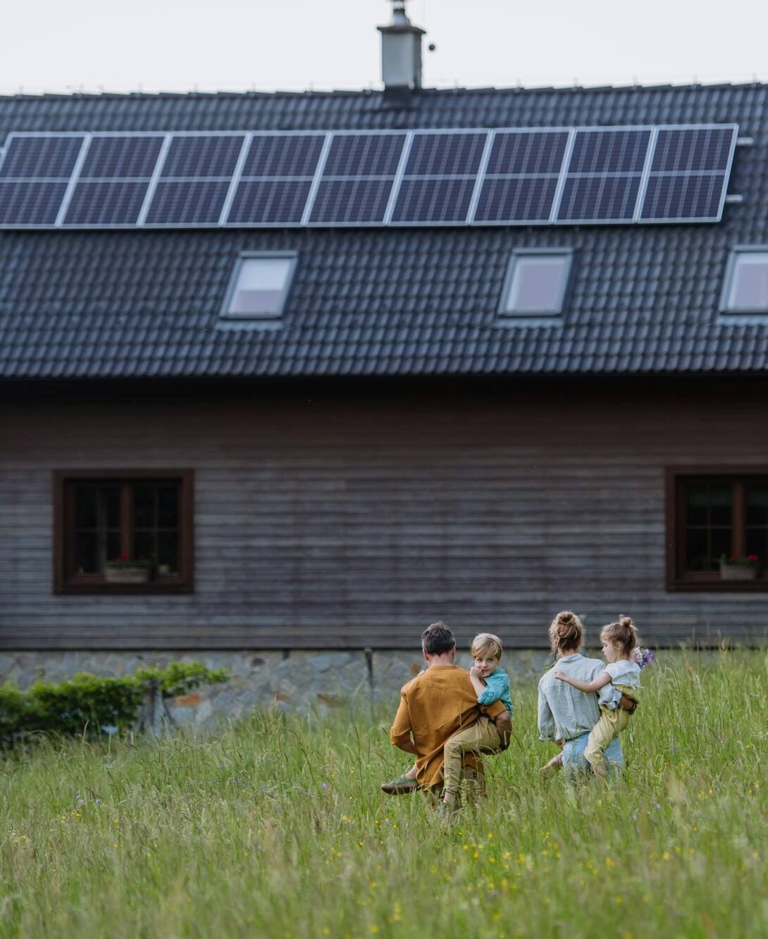 Happy family in front of their house with solar panels on the roof.